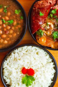Delicious Indian meal featuring curry, rice, and beans garnished with herbs in bowls.