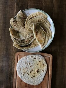 A collection of homemade ghee roti on a ceramic plate with a wooden chopping board.