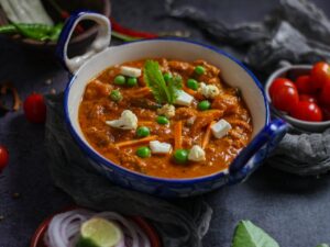 Close-up of vibrant Indian mattar paneer curry with fresh ingredients in a ceramic bowl.
