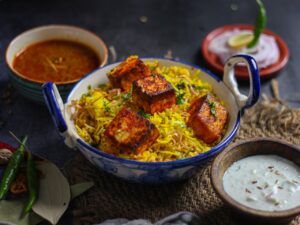 Savor the vibrant flavors of paneer biryani served with traditional Indian sauces in a rustic setting.